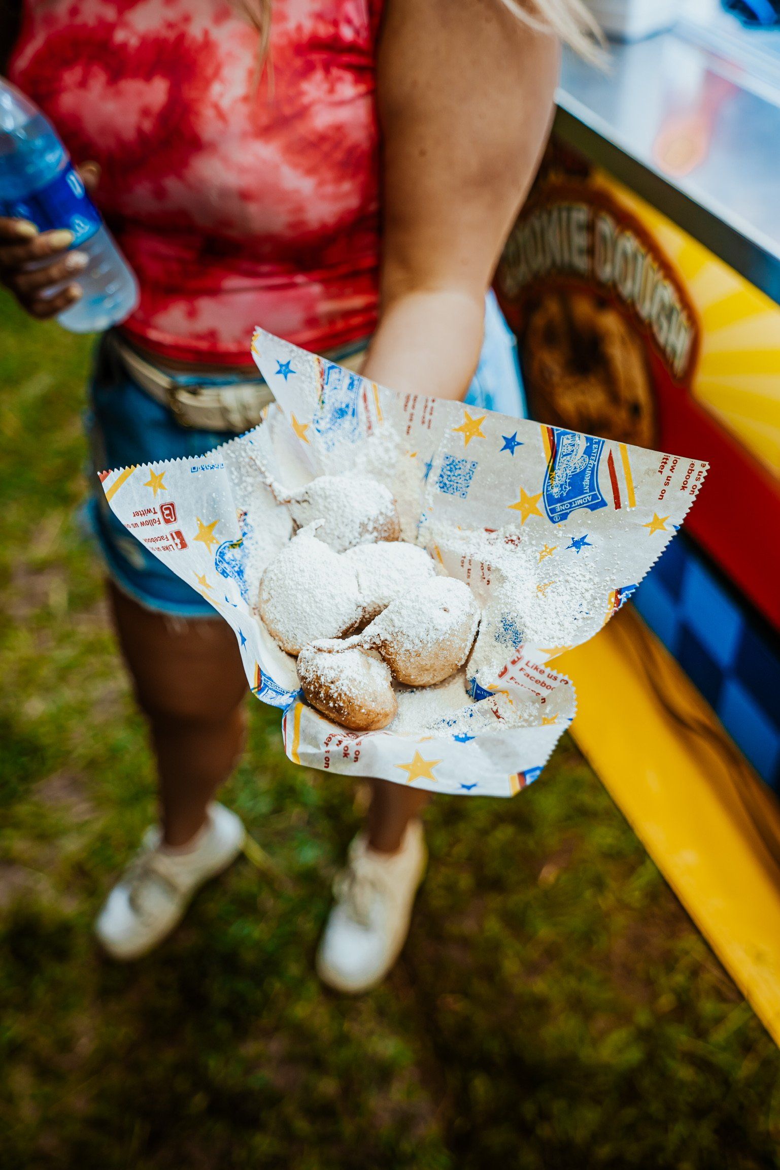 A woman is holding a tray of donuts with powdered sugar.