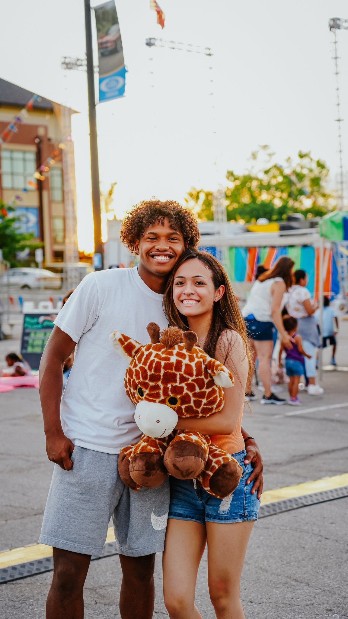 A man and a woman are posing for a picture while holding a stuffed giraffe.