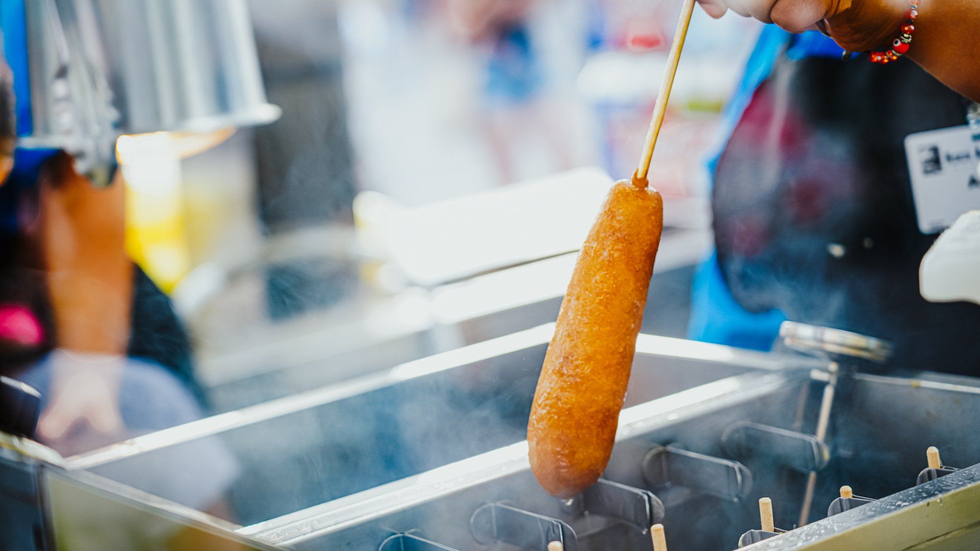 A person is cooking a corn dog on a stick in a fryer.
