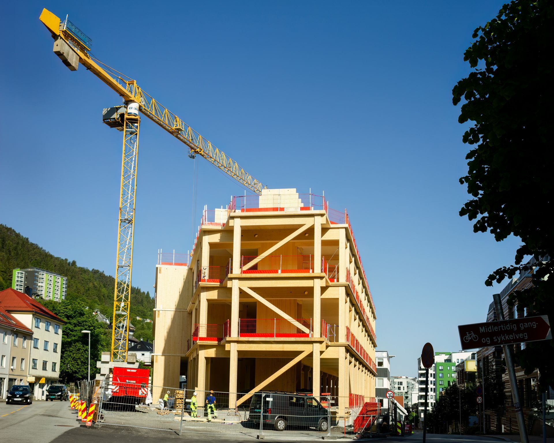 Construction site with a crane building a multi-story wooden building on a city street.