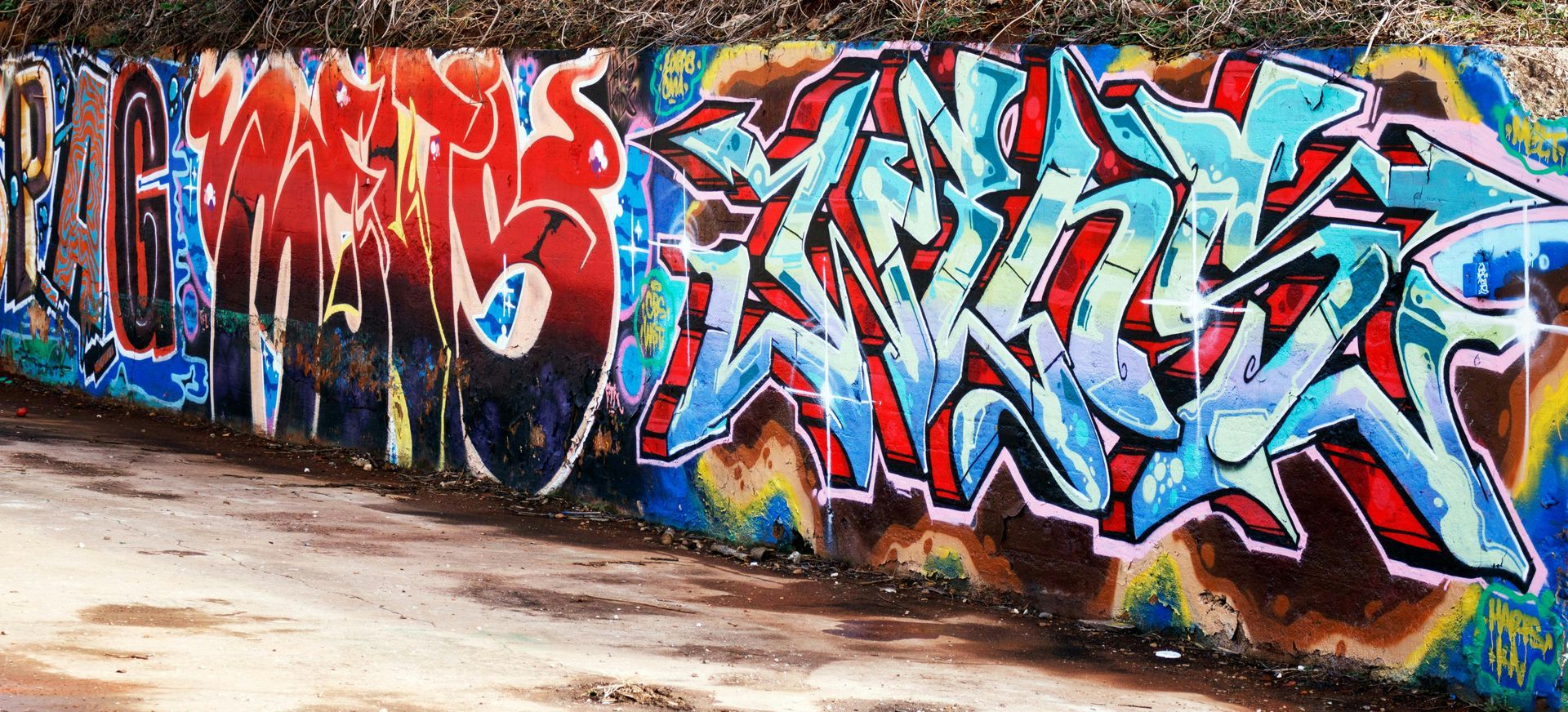 Graffiti on a wall, text in red, blue, and black with a light brown ground.