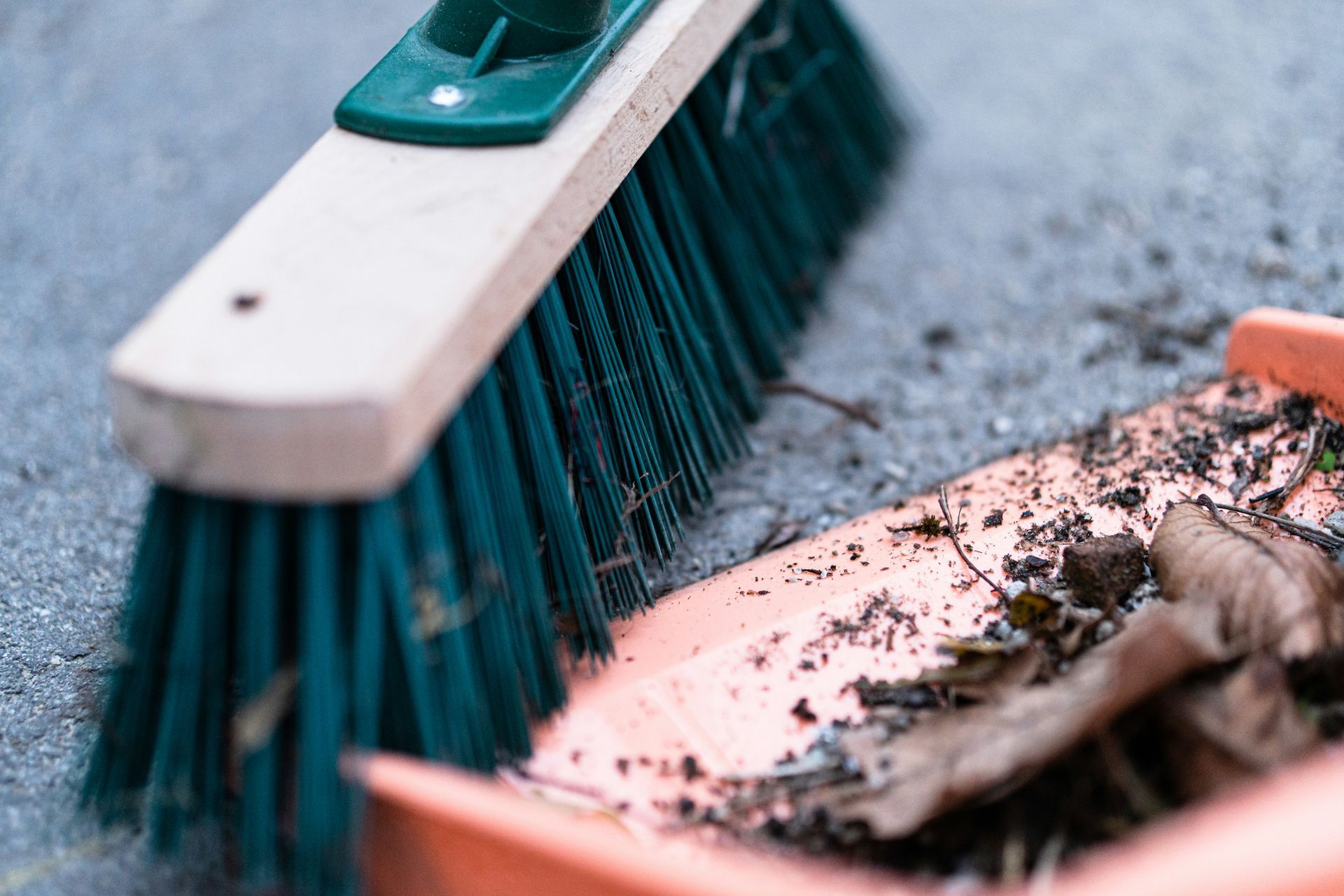 Broom with green bristles and dustpan on gray surface, collecting debris.