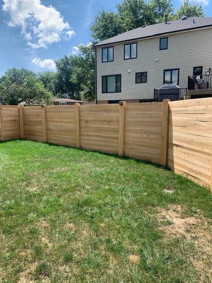 A wooden fence surrounds a lush green yard in front of a house.
