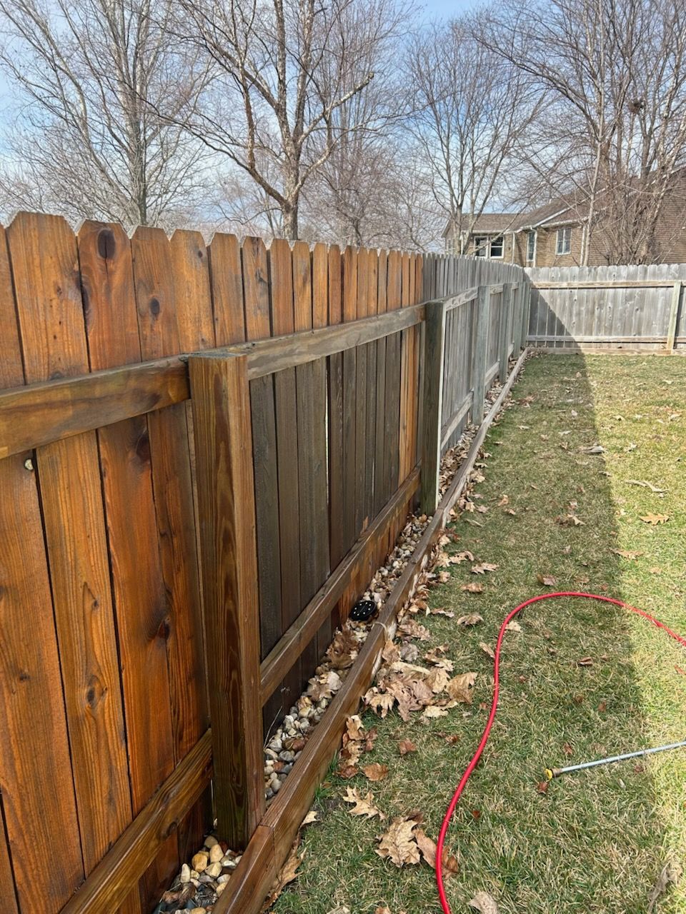 A wooden fence in a backyard with a hose attached to it.