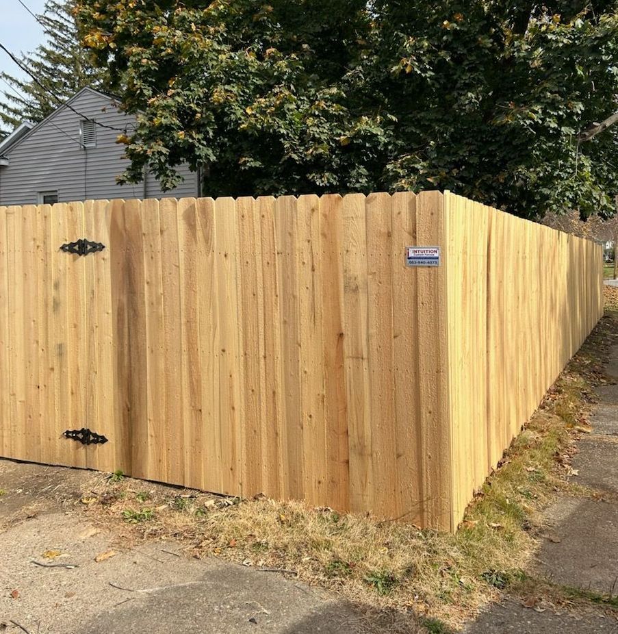 A wooden fence is sitting on the side of the road next to a house.