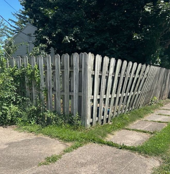 A wooden picket fence along a sidewalk in front of a house