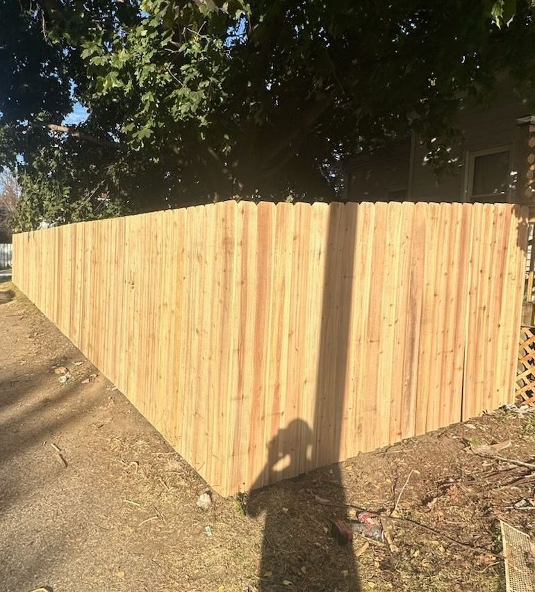 A wooden fence is sitting on the side of a road next to a house.