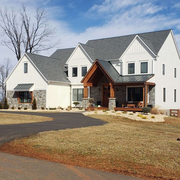 Large white farmhouse with gray roof and wood porch, set beside a curved driveway and winter lawn.
