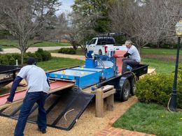 Workers loading a blue utility trailer onto a truck in a residential driveway