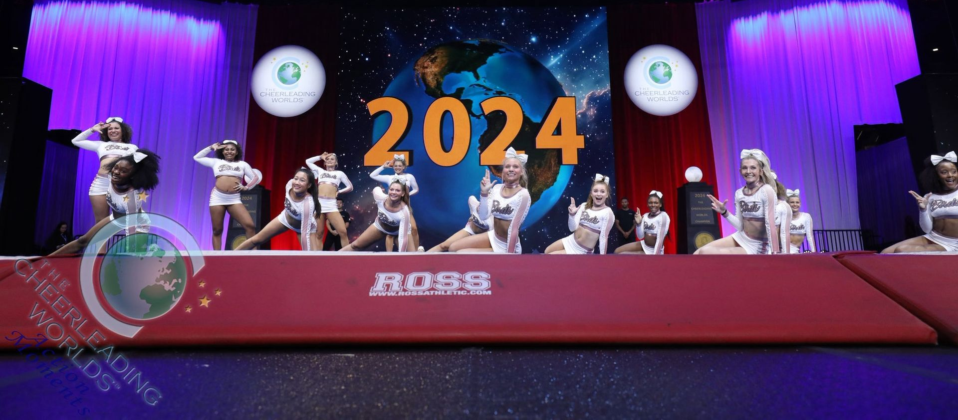 A cheerleading team poses in uniform on a stage in front of a giant globe graphic with the text 