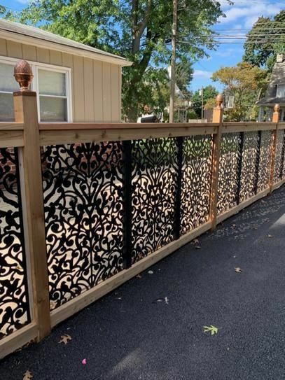 Decorative black metal panel fence with wooden frame, set along a driveway.