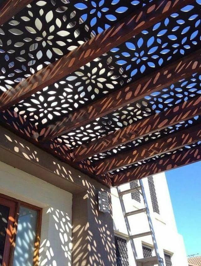 Pergola with floral cutouts casting patterned shadows on a building facade.