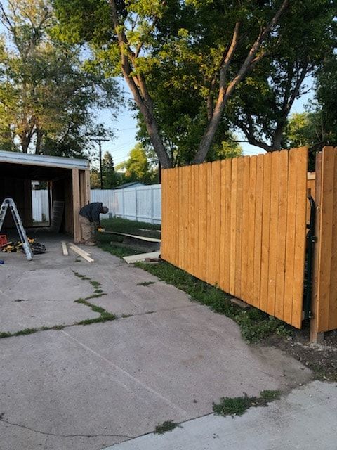 A person working on a wooden fence next to a concrete driveway and garage.