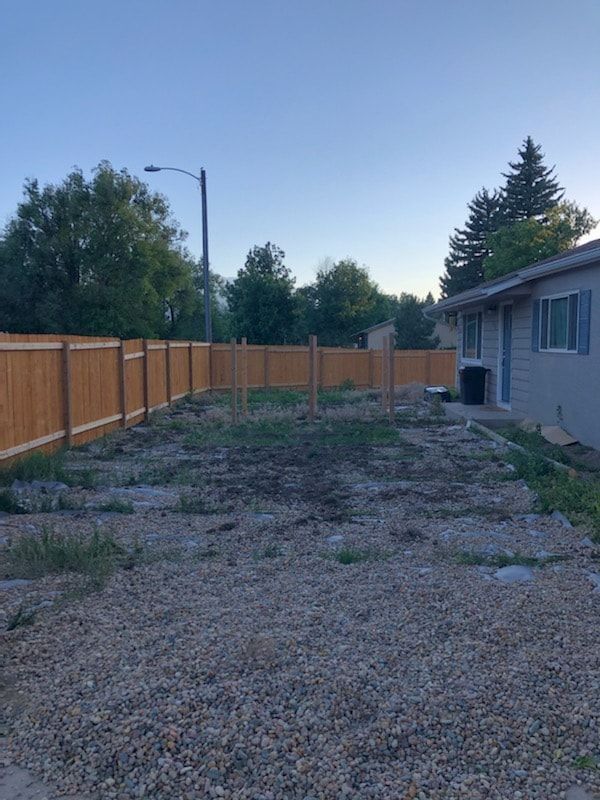 Backyard with a gravel area, dirt patch, unfinished wooden fence posts, and a wood fence against a house.