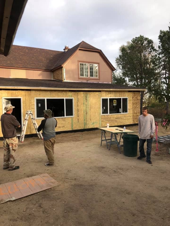 Construction workers outside a building under renovation. Exterior walls are being framed. Cloudy sky overhead.