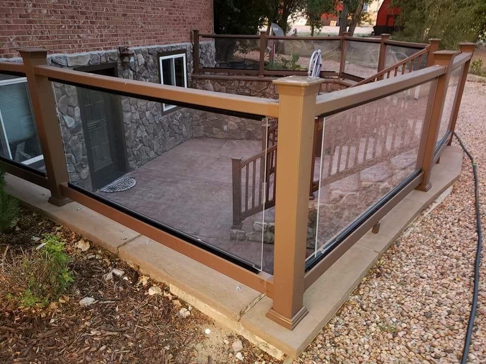 Brown and glass railing surrounds a sunken patio with stone walls and a small staircase.