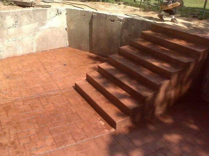 Concrete pool area with stairs and stamped brick pattern floor in shades of brown.