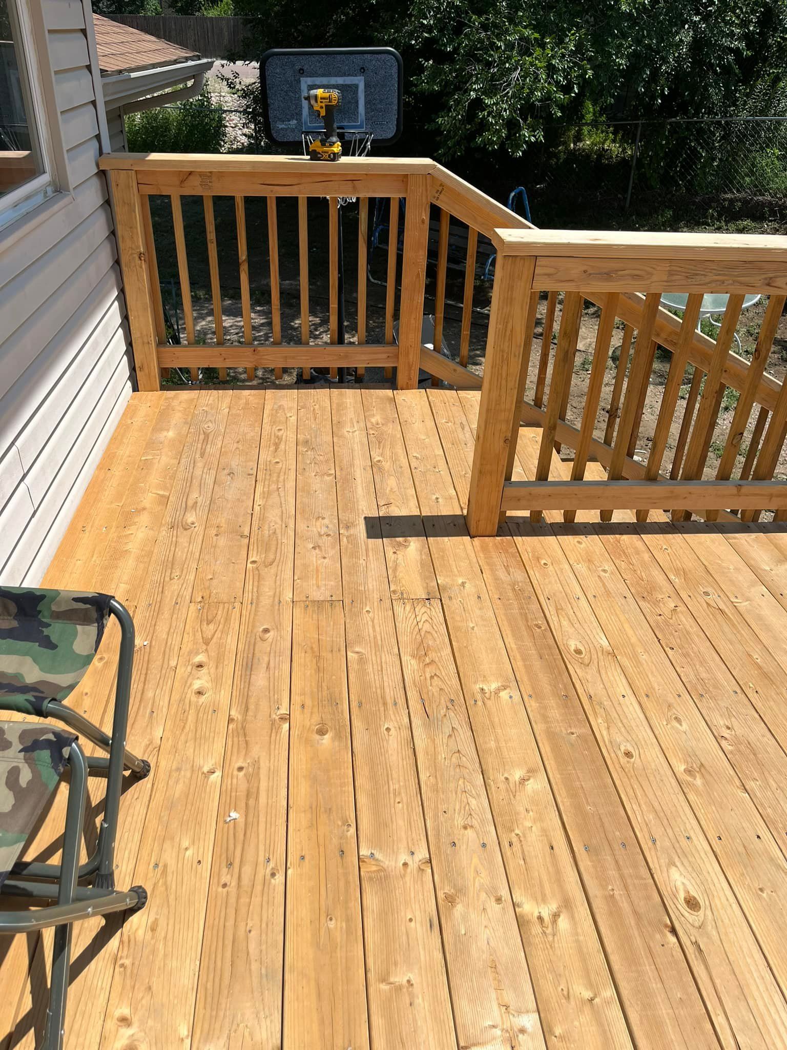 Wooden deck with railing. A camo folding chair sits on the deck. A basketball hoop is visible in the background.
