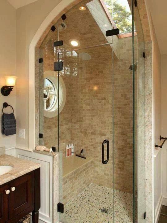 Shower with glass doors, stone tile walls and pebble floor. Features an arched top, round window, and built-in bench.