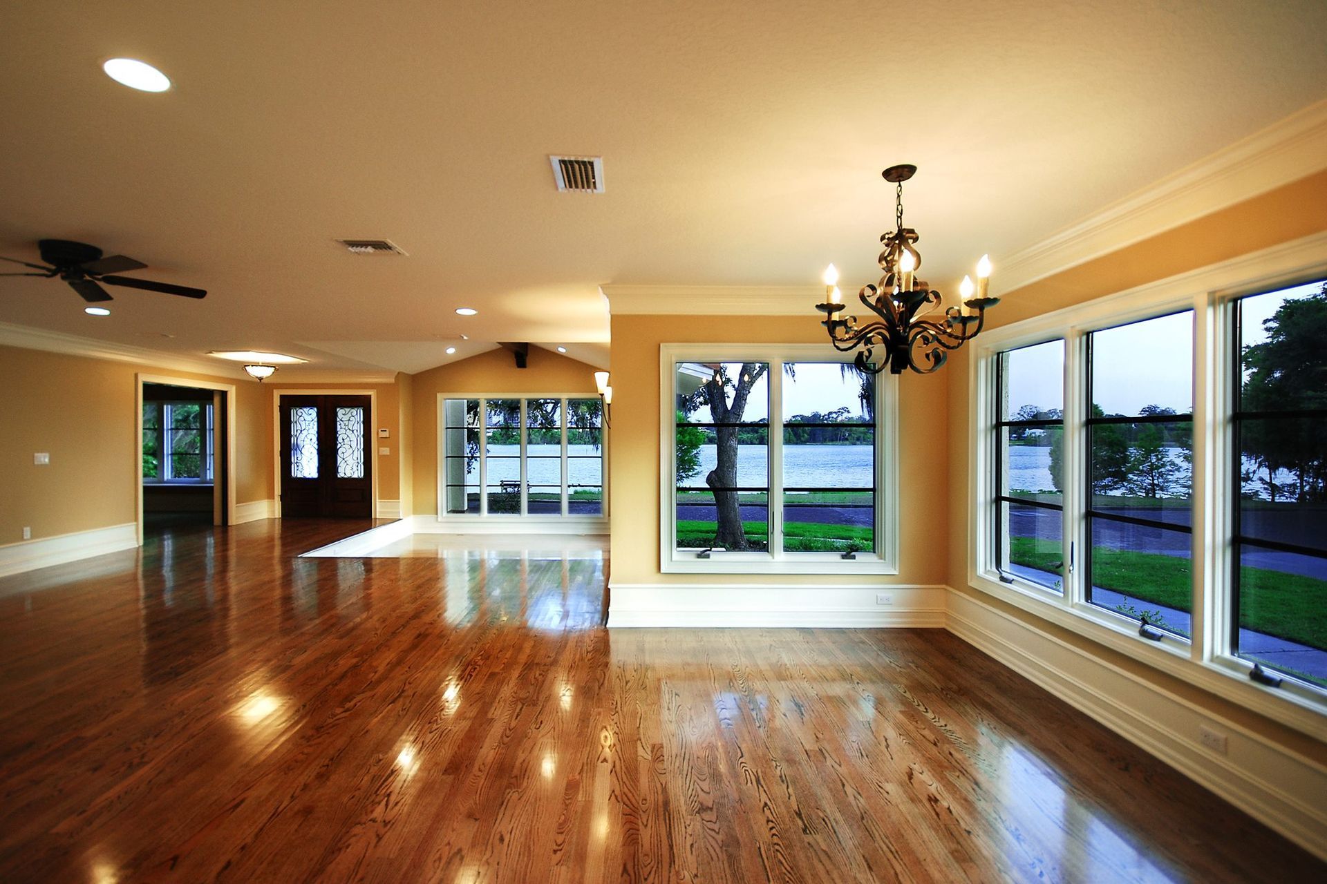 Empty, bright room with wood floors, large windows overlooking water, chandelier.