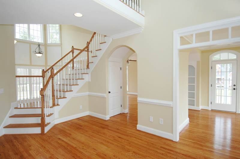 Spacious home interior with wooden floors, staircase, arched doorways, and light yellow walls.