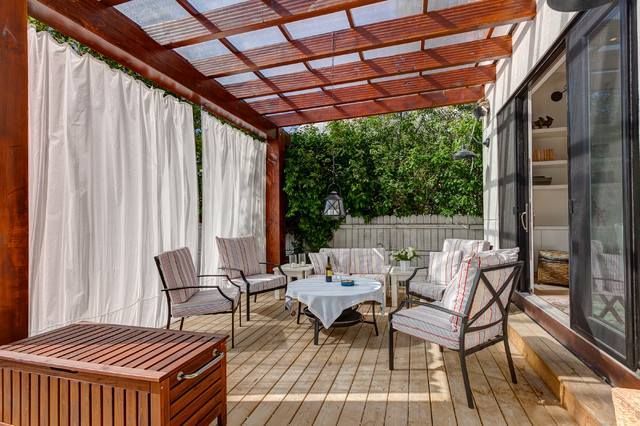 Outdoor patio with wood pergola, white curtains, and seating; a wooden chest sits in the foreground.