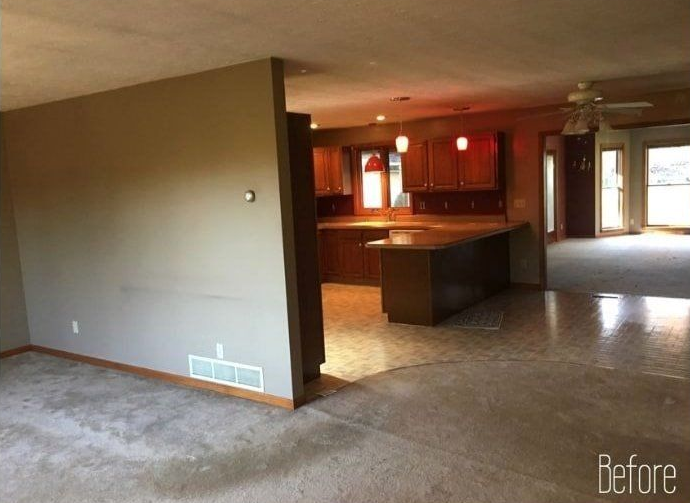 Open-concept kitchen and living room with brown cabinets, island, and wall. Beige carpet and shiny flooring.
