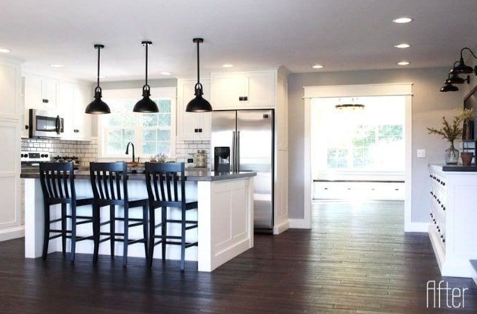 Modern kitchen with white cabinets, dark wood floors, black pendant lights, and island with bar stools.