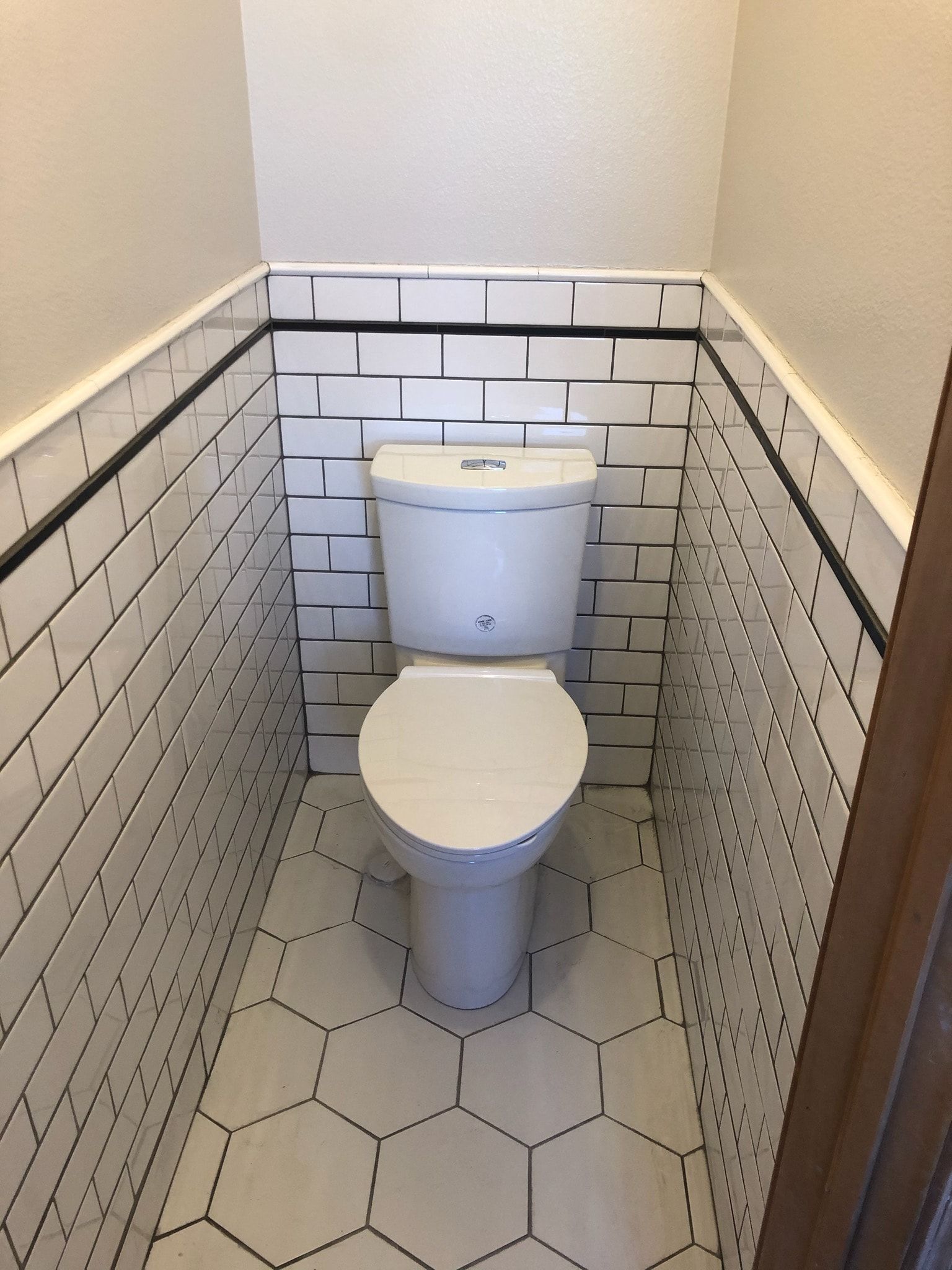 White toilet in a small bathroom with subway tile walls and hexagonal floor tiles.