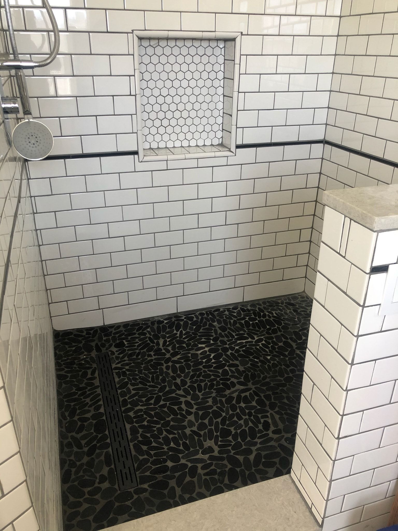 Shower with white subway tile walls, black pebble tile floor, and a built-in shelf.