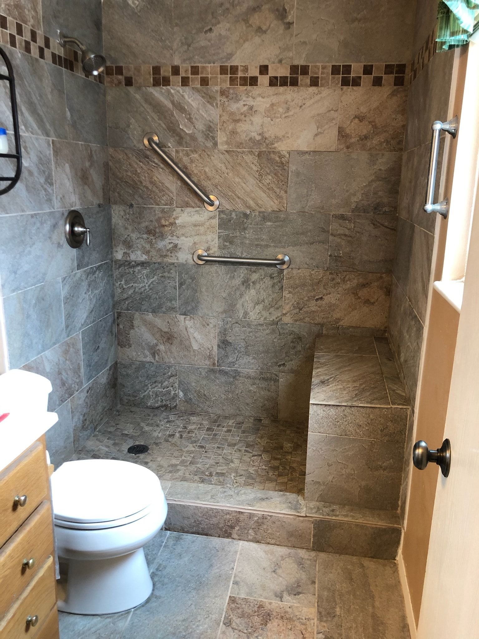 Accessible bathroom with tiled shower, grab bars, and built-in bench. Toilet in front.