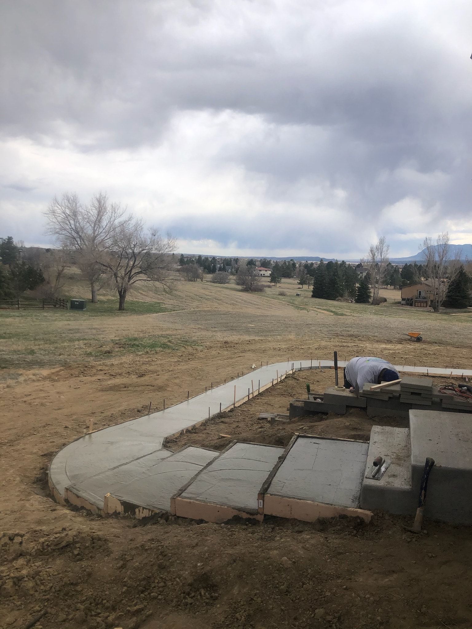 Concrete walkway under construction, leading to a grassy field with cloudy sky.