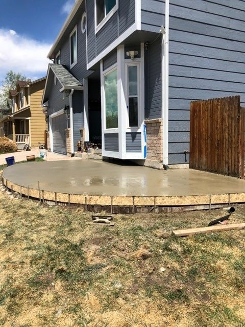 Freshly poured concrete patio next to a two-story blue house with wooden fence and green grass.