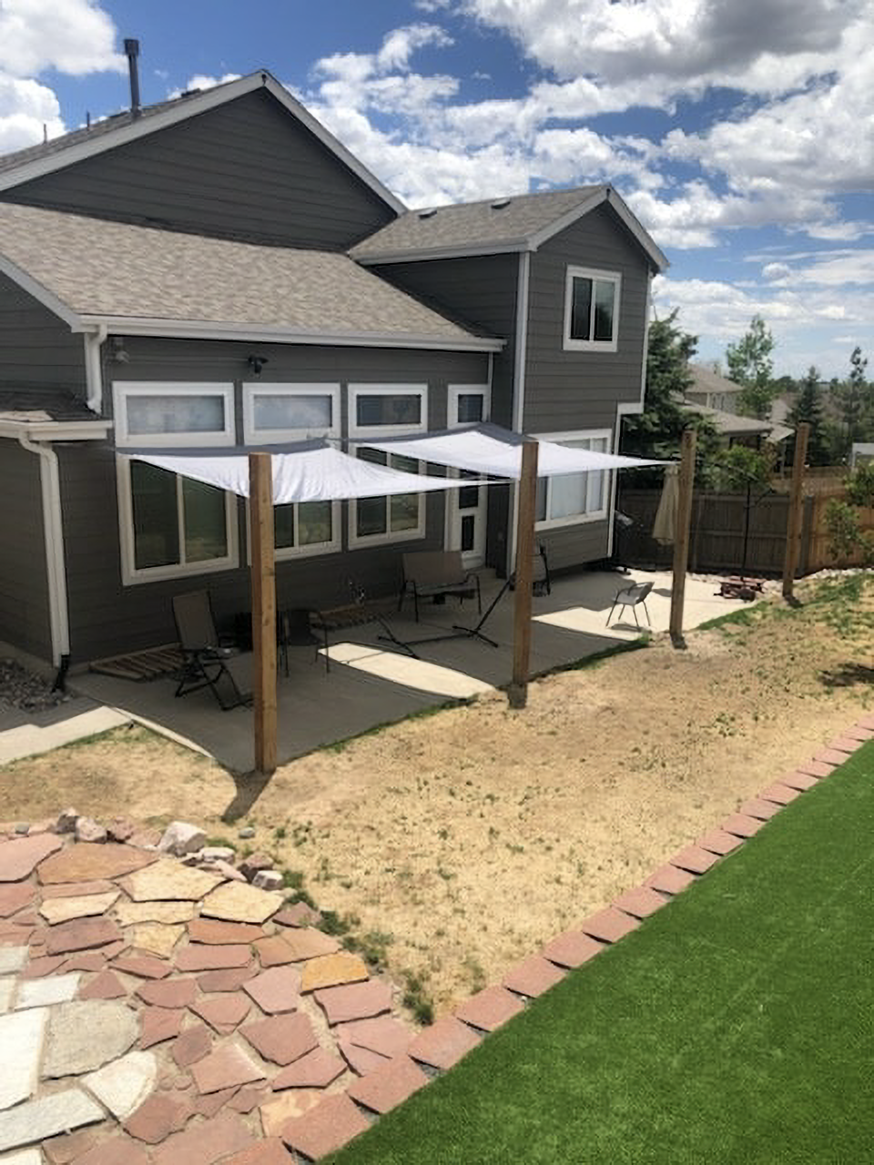 Backyard patio with shade sails, wooden posts, and a two-story house.