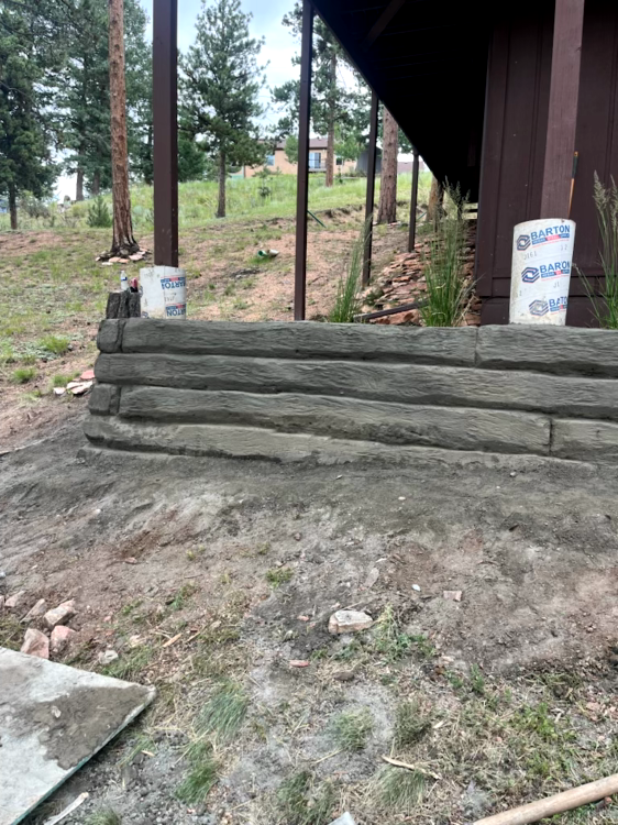 A retaining wall made of concrete logs supporting a sloped yard under a building.