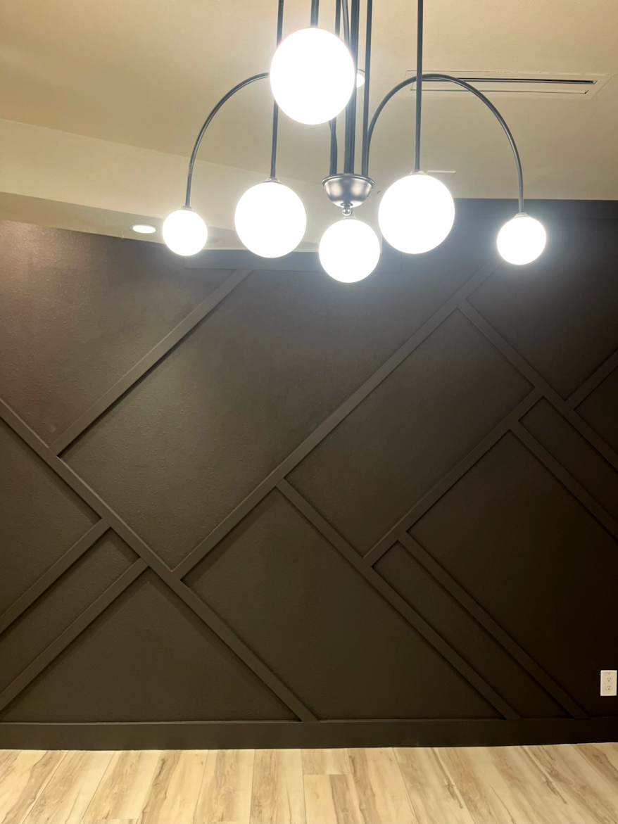 A dark brown accent wall with geometric molding, light fixture with globe lights, and light wood floor.
