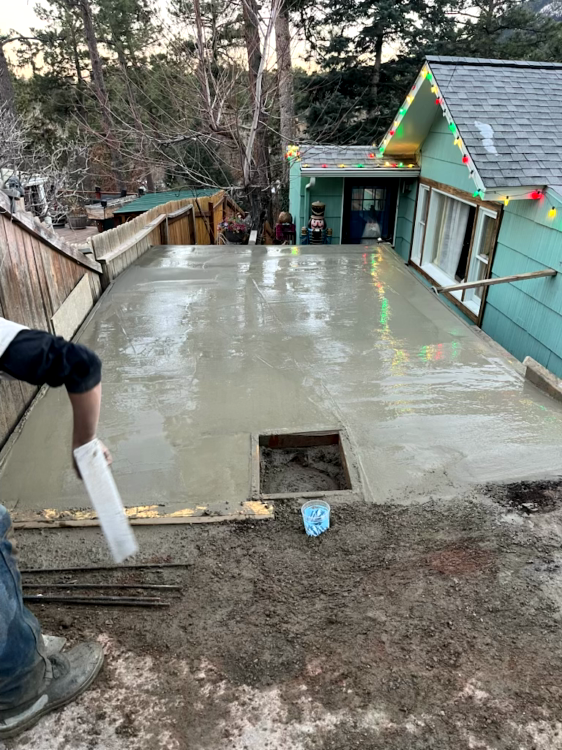 Person smoothing wet concrete on a roof deck, near a light green house with Christmas lights.