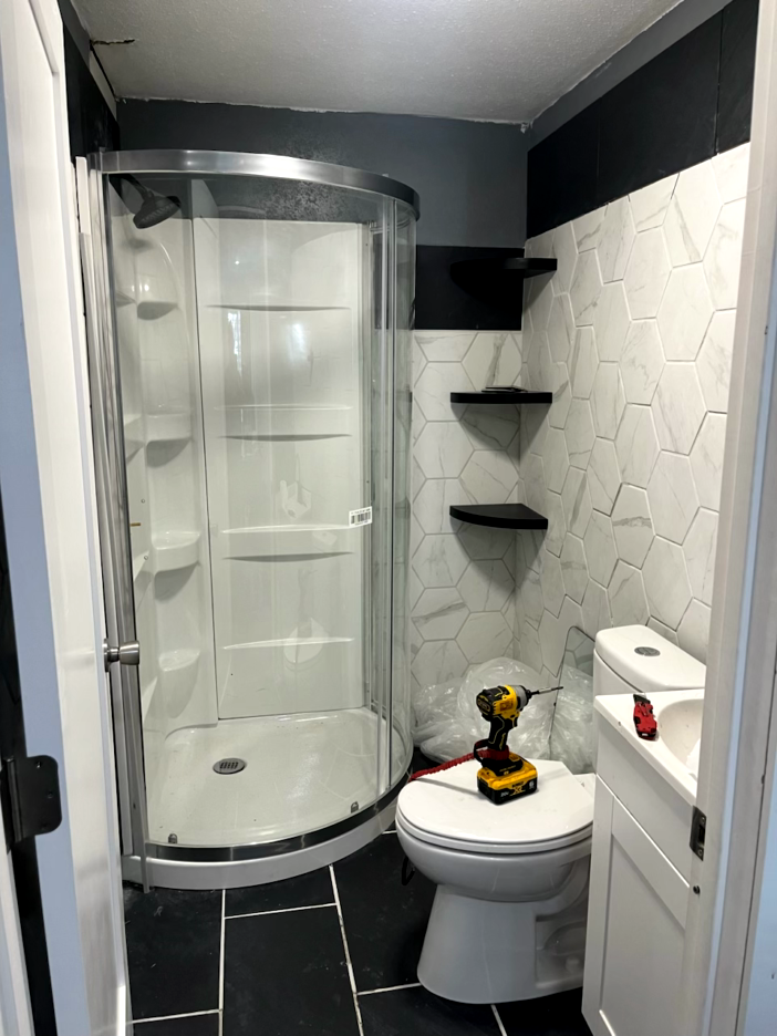 Newly renovated bathroom with a shower, toilet, and shelving. Black and white color scheme.