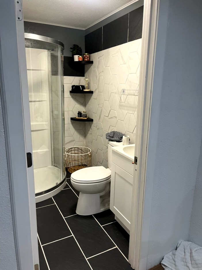 Small bathroom with shower, toilet, and sink; black and white tile; two black shelves.