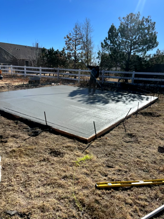 Freshly poured concrete slab in a yard, with a person working on it; bright blue sky overhead.