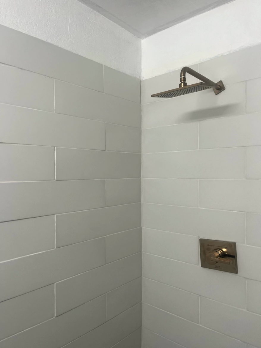A shower stall with white rectangular tiles and a bronze shower head and control.
