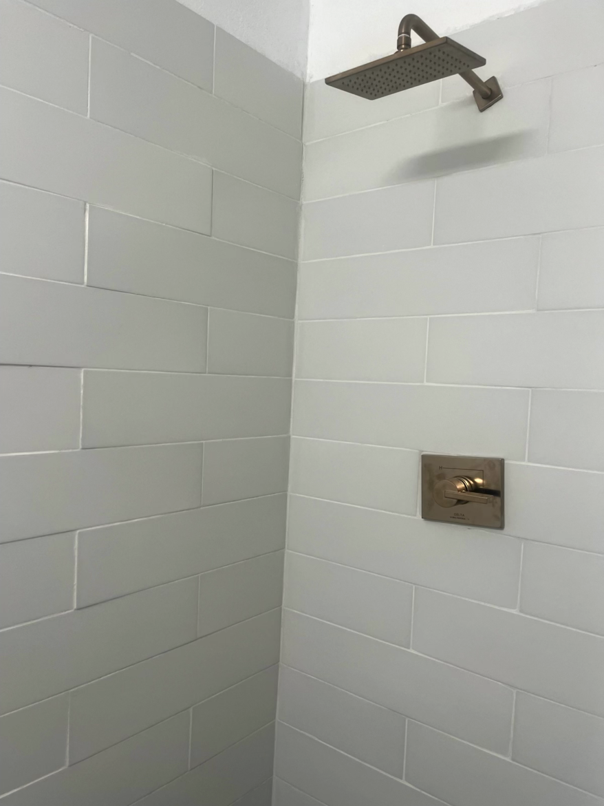 Shower stall with rectangular gray tiles, a bronze showerhead and faucet.