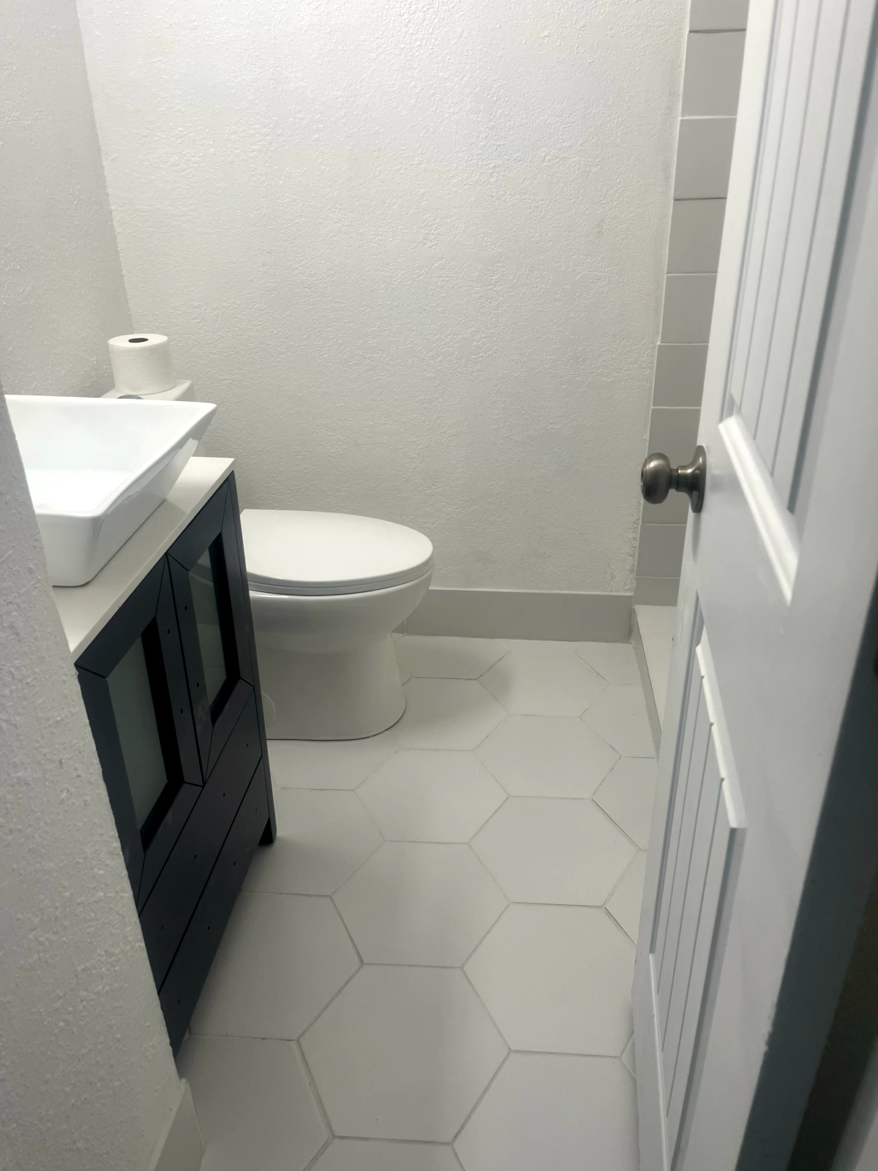 Small bathroom with white hexagonal floor tiles, a toilet, and vanity with a sink.