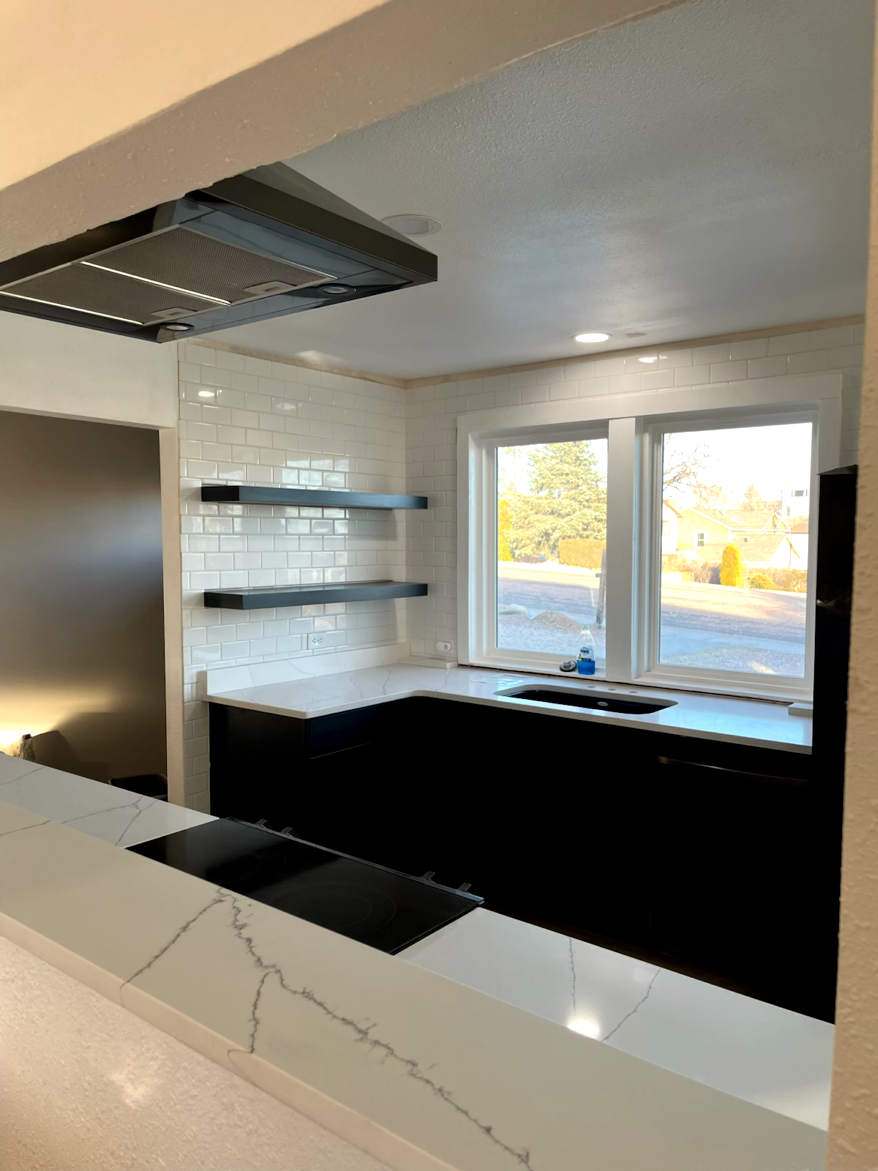 Modern kitchen remodel with black cabinets, white countertops, and subway tile backsplash. Open shelving and window.