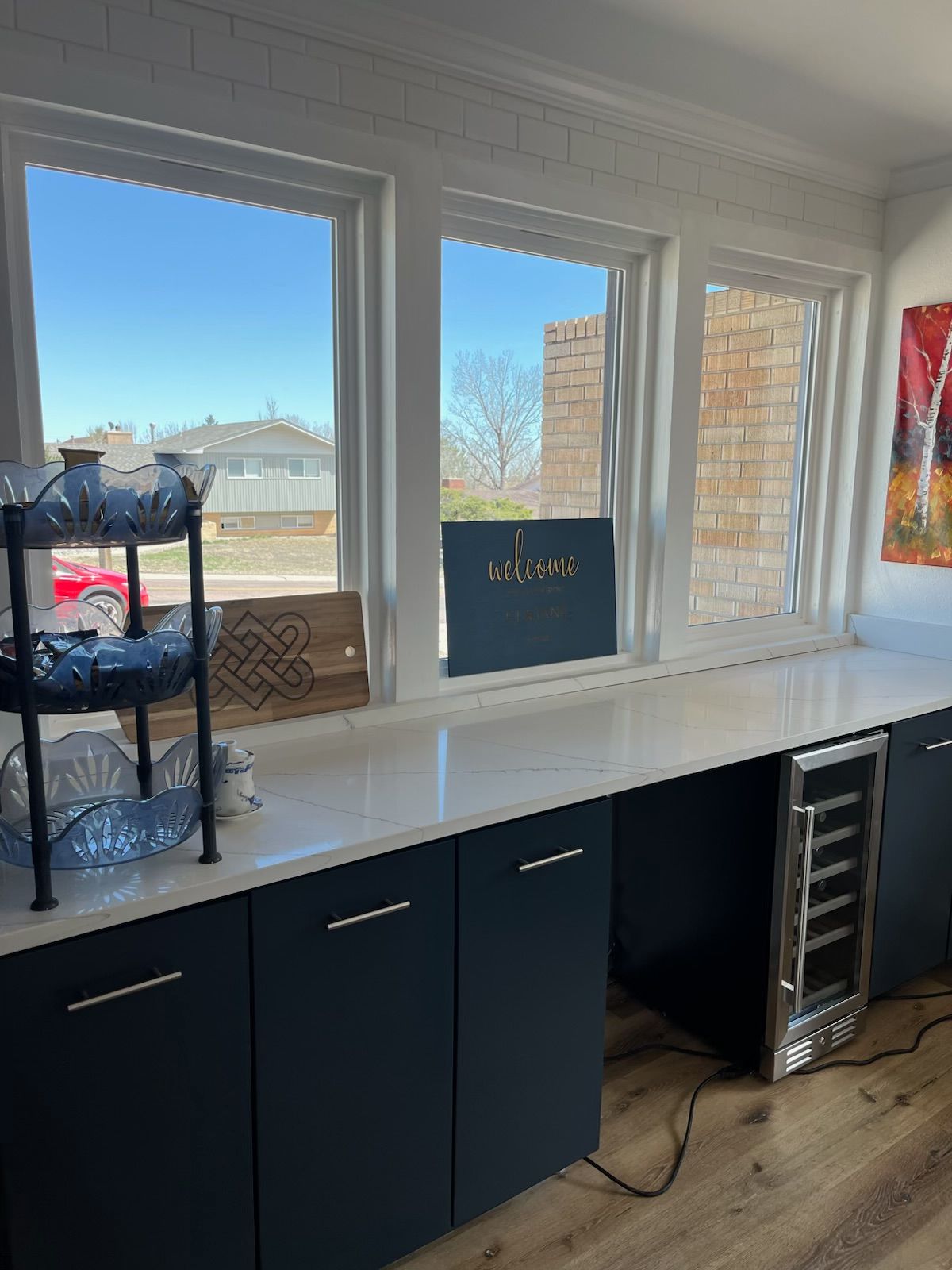 A modern kitchen with a countertop, cabinets, and windows overlooking a neighborhood.