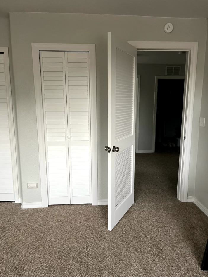 Bedroom with open white louvered door, a closed bi-fold closet, and neutral carpet.