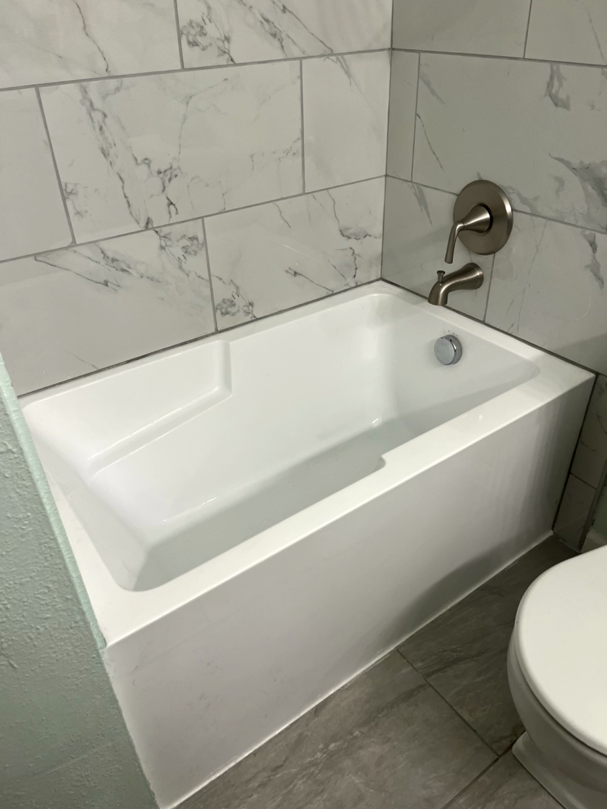 White bathtub with silver fixtures in a bathroom with marble-look tile walls and gray floor tiles.
