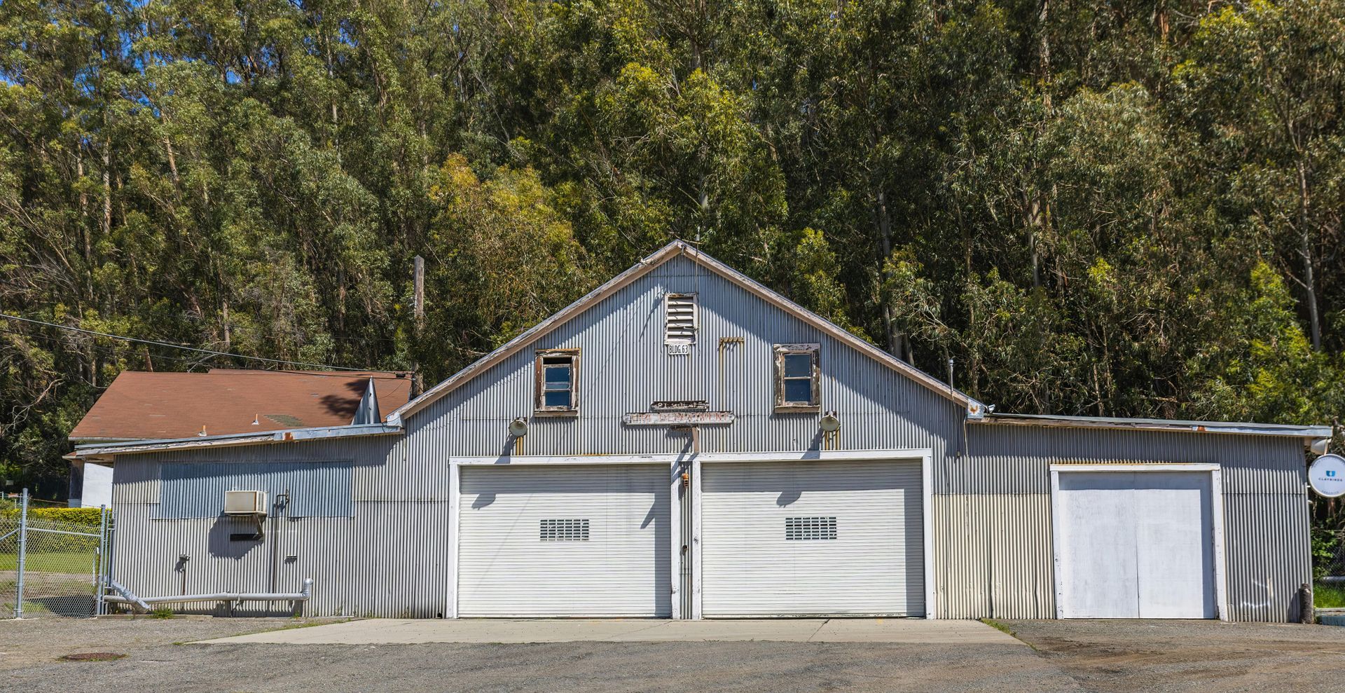 Metal-sided building with two garage doors and a smaller side door, set against a backdrop of trees.