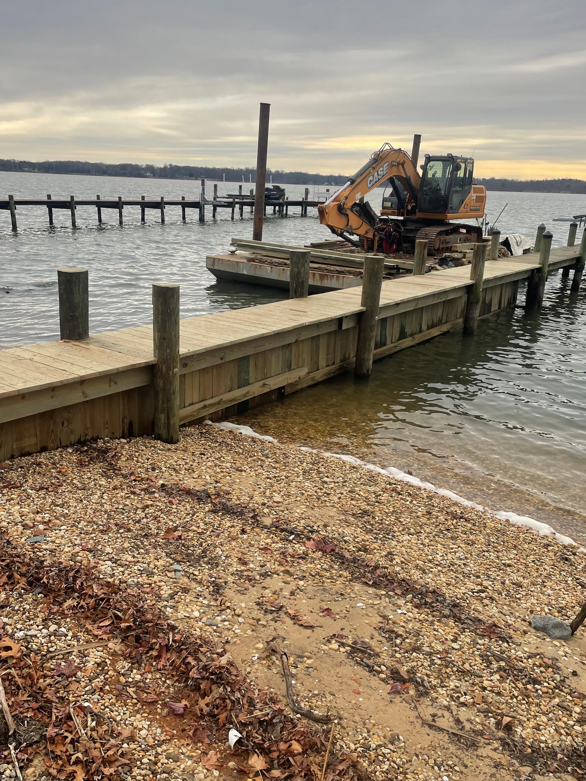 A large excavator is sitting on a dock next to a body of water.