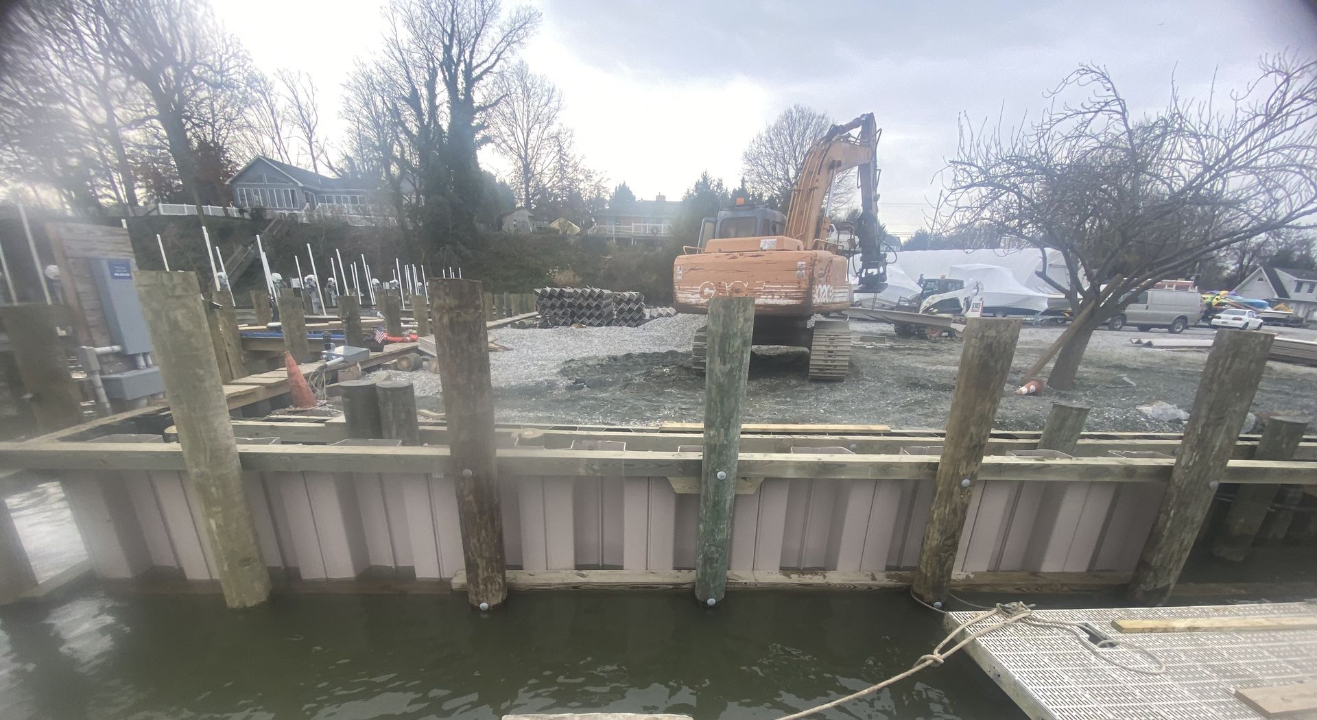 A large orange excavator is working on a construction site next to a body of water.